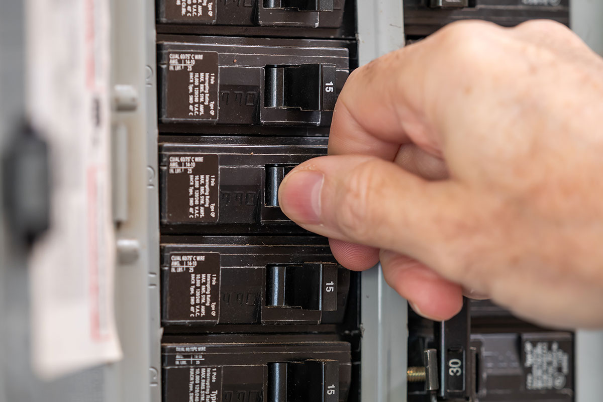 Picture of an electrical panel with a mans hand operating one of the breakers. This is a more modern electrical panel replacement.